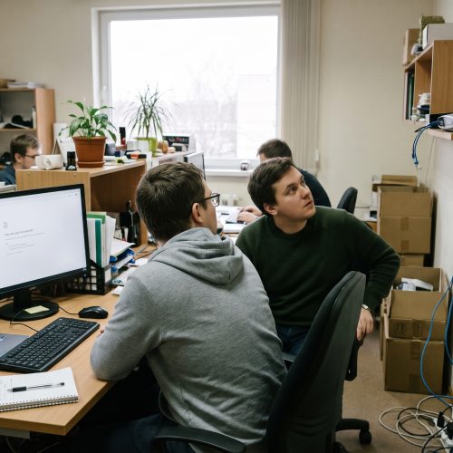 Deux personnes vérifient un message d’erreur réseau sur un écran et un routeur posé sur une étagère dans un bureau.