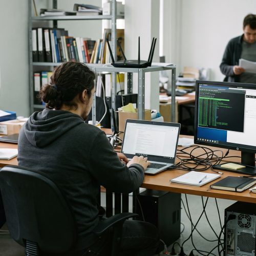 Une personne travaille sur un terminal SSH dans un bureau partagé, avec écran externe, routeur et câbles visibles.